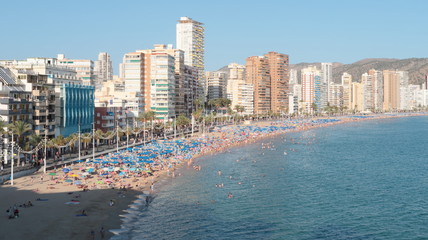 Playa de levante llena de personas en la arena tomando el sol y bañandose en el agua del mar