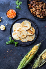 COLOMBIAN FOOD. Maize AREPAS and fried pork chicharron ans colombian tomato sauce. Top view. Black background