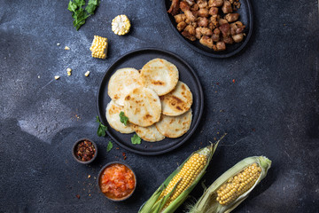 COLOMBIAN FOOD. Maize AREPAS and fried pork chicharron ans colombian tomato sauce. Top view. Black background