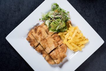 Chicken schnitzel, served with fries and salad. Natural wooden background.