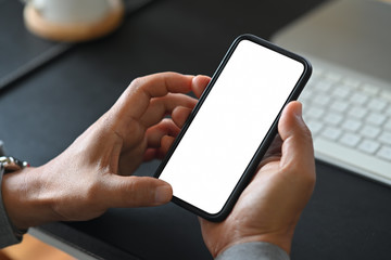 Man's hand holding white screen mobile phone on desk in office