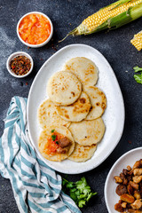 COLOMBIAN FOOD. Maize AREPAS and fried pork chicharron ans colombian tomato sauce. Top view. Black background