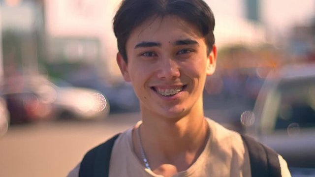 Happy asian guy laughing at camera, close-up standing on the street, cars and road on the background, city life