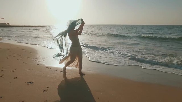 sensual joyful girl are walking on seashore, playing with vivid silk cloth