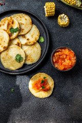 COLOMBIAN FOOD. Maize AREPAS and fried pork chicharron ans colombian tomato sauce. Top view. Black background
