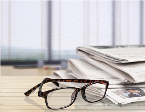 Newspapers with reading glasses on background