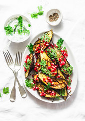 Roasted eggplant with feta, greek yogurt, cilantro sauce and pomegranate seeds on light background, top view. Delicious snack, tapas, appetizers