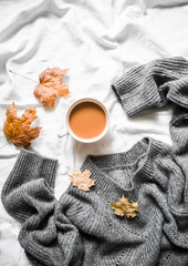 Cup of coffee, gray warm knitted sweater oversize, yellow dry leaves on the bed - cozy home still life, top view
