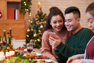 Happy young Vietnamese couple reading messages on smartphone screen