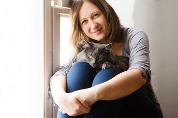 Young woman playing with cat about a window in home.