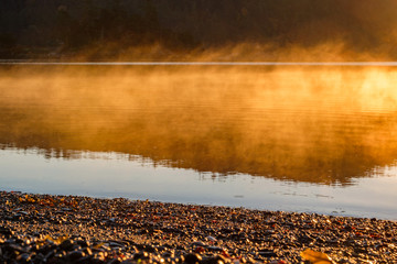 morning mist above the lake illuminated by the orange sunlight