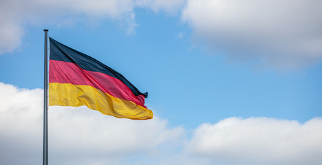 German flag waving on flagpole. Cloudy blue sky background, copyspace, banner.