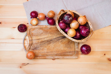 Colorful onions in basket and cutting board on wooden background. Top view, copy space.