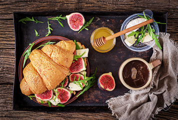 Fresh croissant sandwich with  brie cheese arugula and figs. Delicious breakfast.  Tasty food. Flat lay. Top view