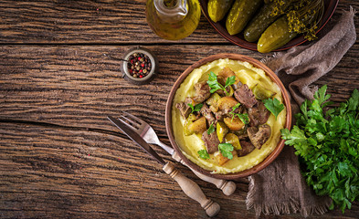 Fried chicken liver with apples, sweet pepper and onions with mashed potatoes as close-up in a bowl on wooden table. Top view. Flat lay.