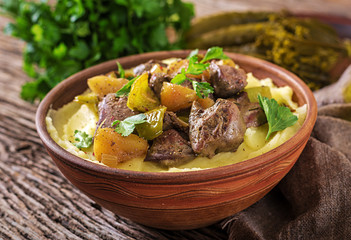 Fried chicken liver with apples, sweet pepper and onions with mashed potatoes as close-up in a bowl on wooden table.