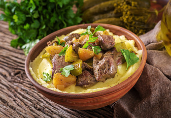 Fried chicken liver with apples, sweet pepper and onions with mashed potatoes as close-up in a bowl on wooden table.