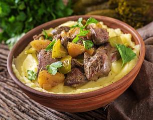 Fried chicken liver with apples, sweet pepper and onions with mashed potatoes as close-up in a bowl on wooden table.