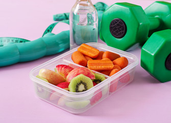 Fitness equipment. Healthy food. Concept healthy food and sports lifestyle. Vegetarian lunch. Dumbbell, water, fruits on pink background.