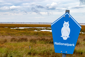 blue sign of a german national parc on front of a coastline with german lettering "nationalpark" means national parc