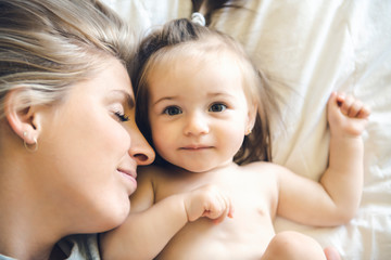 Mother and his baby daughter on bed having fun