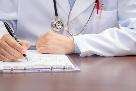 A male doctor writing on the medical form with the stethoscope nearby.