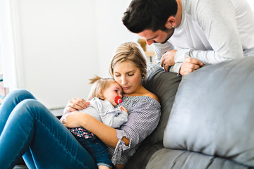 Young family with baby daughter on sofa at home, the baby crying