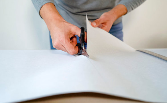 closeup male hands preparing new bended wallpaper roll with scissors on table indoor. Cutting preparation in repair apartment. renovation, design concept