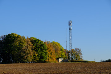 Handy Sendemast vor herbstlicher Hecke, Feld im Vordergrund