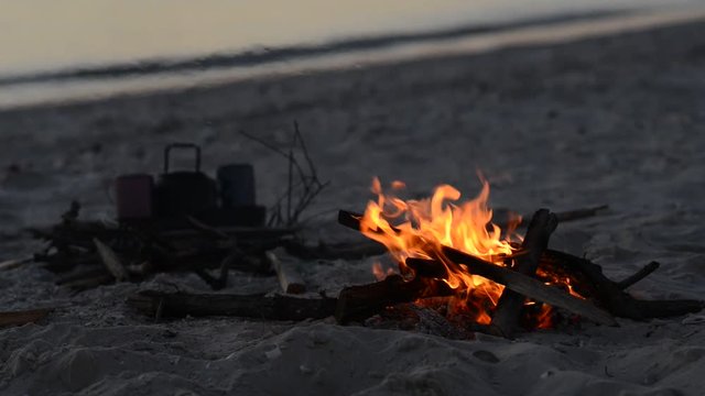 Bonfire burns on the beach next to waves during sunset. Amazing travel to the seashore.
