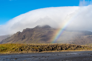 Mountain covered in a white cloud with a rainbow across the scene