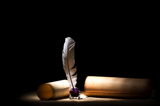 Literature concept. Old inkstand with feather near scrolls against black background. Dramatic light and free space