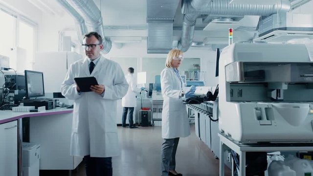 Team of Research Scientists Working On Computer, with Medical Equipment, Analyzing Blood and Genetic Material Samples with Special Machines in the Modern Laboratory.