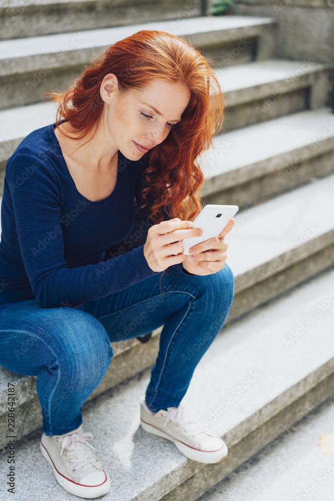 Wall mural Young woman sitting on steps with mobile phone