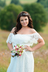 Beautiful brunette girl with a bouquet of flowers. Young woman with long hair in a white lace dress. Summer female portrait