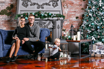 Happy family having fun at home. Christmas morning in loft room with brick wall. Young parents with little son. father, mother and their baby boy. Happy new year. decorated Christmas tree