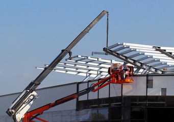 Naklejka premium Cherry picker and a telescopic crane at work for the installation of roof metallic frame on a new building