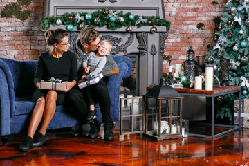 Obraz na płótnie Canvas Happy family having fun at home. In loft room with brick wall. Young parents with little son. father, mother and their baby boy. Happy new year. decorated Christmas tree