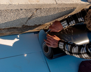 Worker with a heat gun is welding PVC sheets for waterproofing a terrace. Selective focus