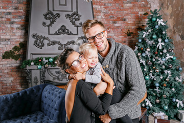 Happy family having fun at home. In loft room with brick wall. Young parents with little son. father, mother and their baby boy. Happy new year. decorated Christmas tree