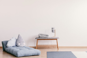 Futon with cute pillows on the floor of stylish baby room interior with copy space on the empty white wall © Photographee.eu