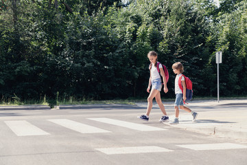 Girl and boy with backpacks walking on pedestrian crossing from the school