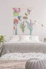 Fabric with flowers hanging on white wall in bright bedroom interior with metal lamp, double bed...