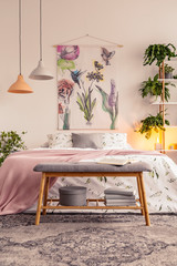 Bench with grey box and books standing by the bed with floral bedclothes and pastel pink blanket in...