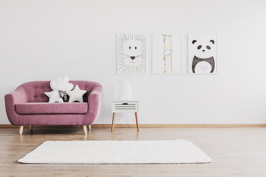 Stylish pink couch with cute pillows in spacious baby room interior with animals posters on the wall