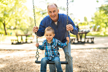 A Grandfather pushing his grandson on the rope swing - obrazy, fototapety, plakaty
