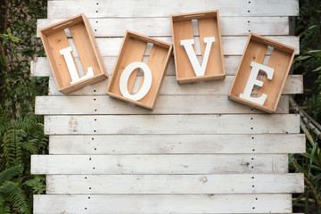 Close up love in the box. letter word the character l,o,v,e in wood box are hanging on the white wood wall.symbol of valentine day and love. romantic decoration.