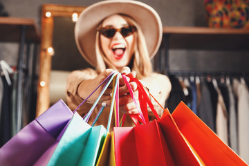 Rich pretty blonde shopaholic woman wearing sunglasses and fashion hat holding many colorful shopping bags in fashion mall, concept of consumerism, Black Friday, sale, rich life