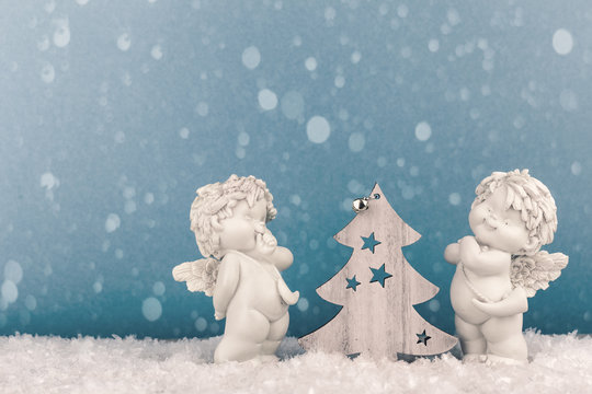 Two Christmas Baby Angels Statuettes On Snow With Christmas Tree