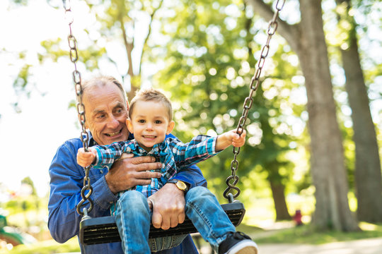 A Grandfather Pushing His Grandson On The Rope Swing